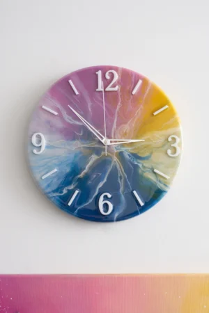 Zegar o białej tarczy z kolorowymi wirami w odcieniach niebieskiego, żółtego i różowego
