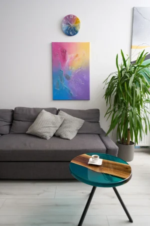 Zestaw rękodzieł składający się ze stolika kawowego i zegara wykonanych z żywicy epoksydowej, oraz abstrakcyjnego obrazu.